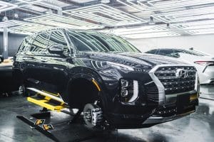 A black Hyundai Palisade SUV parked in a garage with its wheels removed. The SUV appears to be undergoing repairs, suggesting potential engine issues.