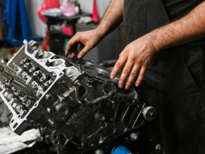 Mechanic using engine reconditioning equipment on a cylinder head in a workshop.