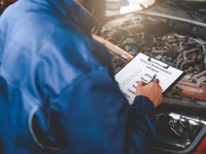 Mechanic inspecting vehicle maintenance checklist while checking old car engines for regular service and upkeep.