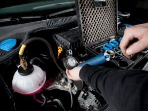 Mechanic testing cooling system pressure of old car engines using specialised equipment during routine maintenance.